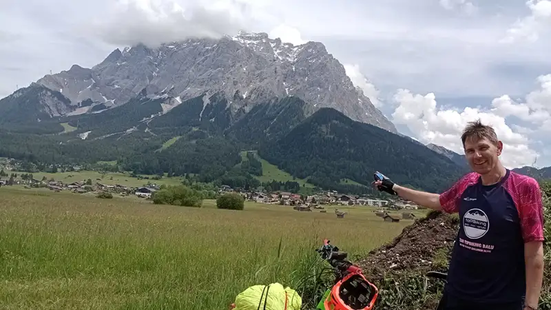 Christian Waniaus beim Alpencross, er deutet mit dem Finger auf einen großen Berg hinter sich