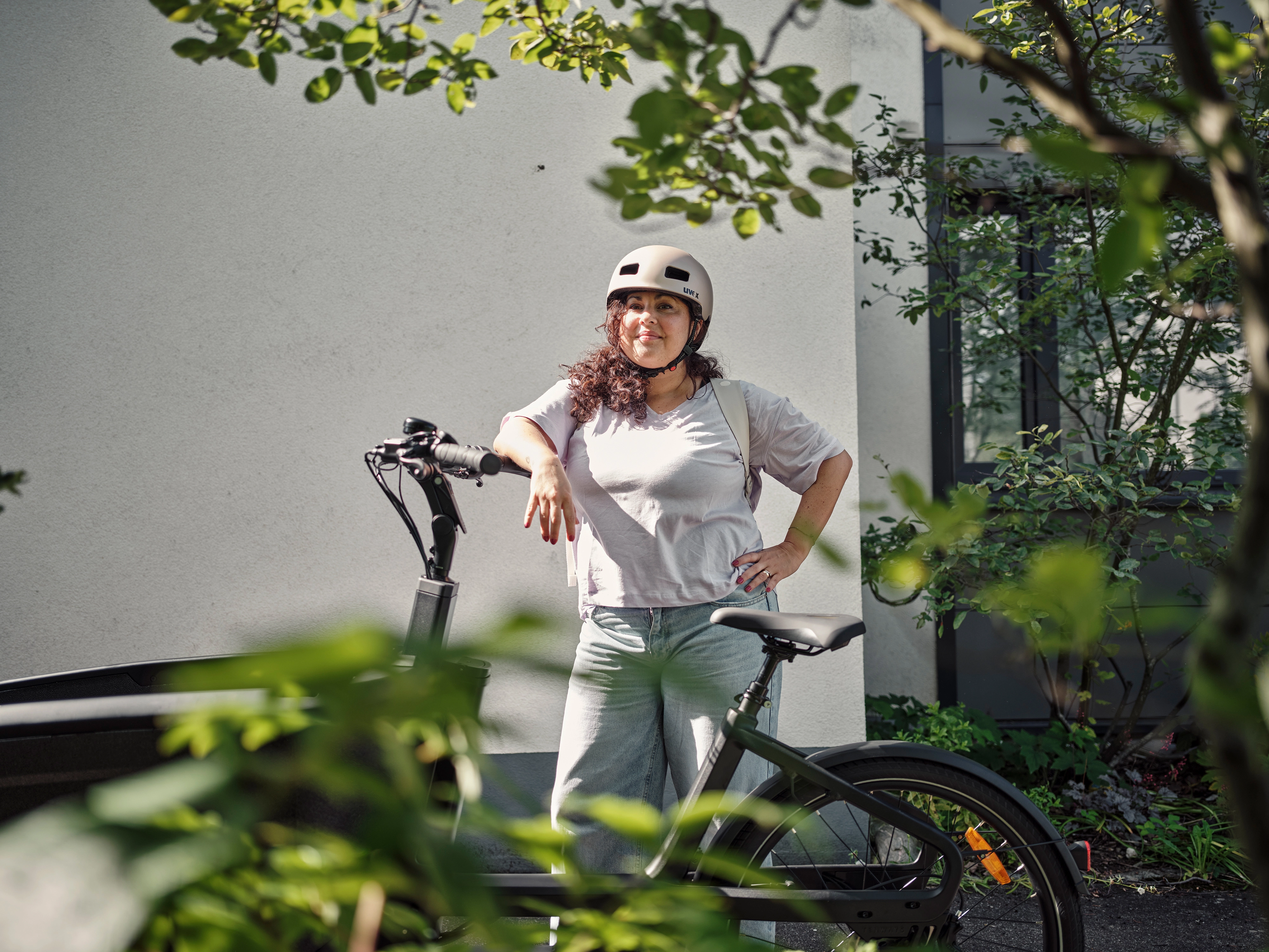 Eine Frau lehnt stolz an ihrem Lastenrad und trägt einen Helm. Eine Frau lehnt stolz an ihrem Lastenrad und trägt einen Helm.